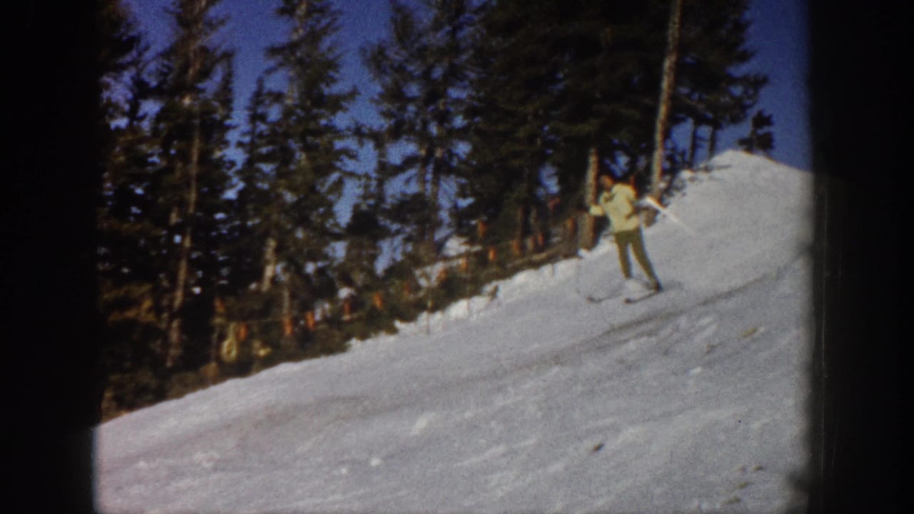 A light-jacketed skier pauses or turns on a snowy Aspen slope, framed by tall evergreens and home-movie film edges.