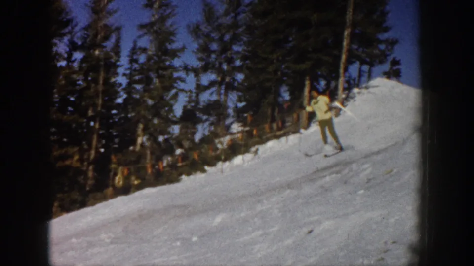 A light-jacketed skier pauses or turns on a snowy Aspen slope, framed by tall evergreens and home-movie film edges.