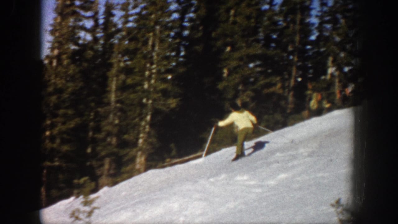 In 1961 Aspen, Colorado, a woman in a light jacket practices skiing on a snow-covered slope bordered by evergreens.