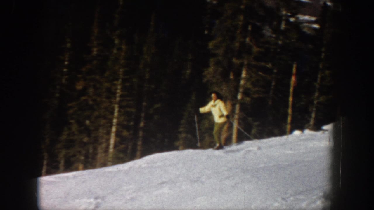 1961 Aspen home-movie frame showing a lone skier with poles on a snowy slope beside dark evergreen forest.