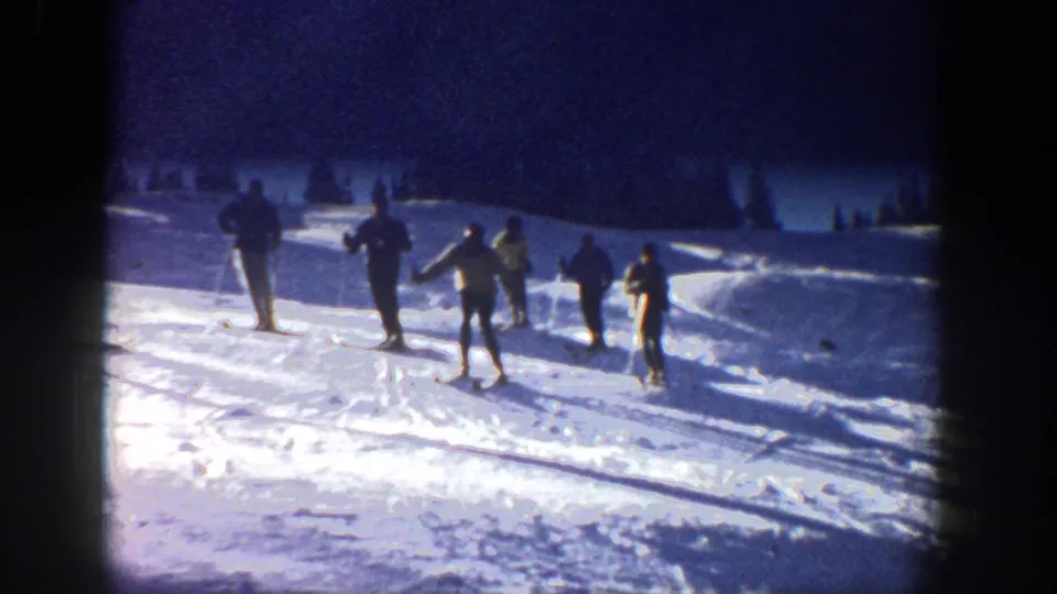 1961 Aspen frame showing a small group of skiers with poles on a sunlit snowy practice slope.