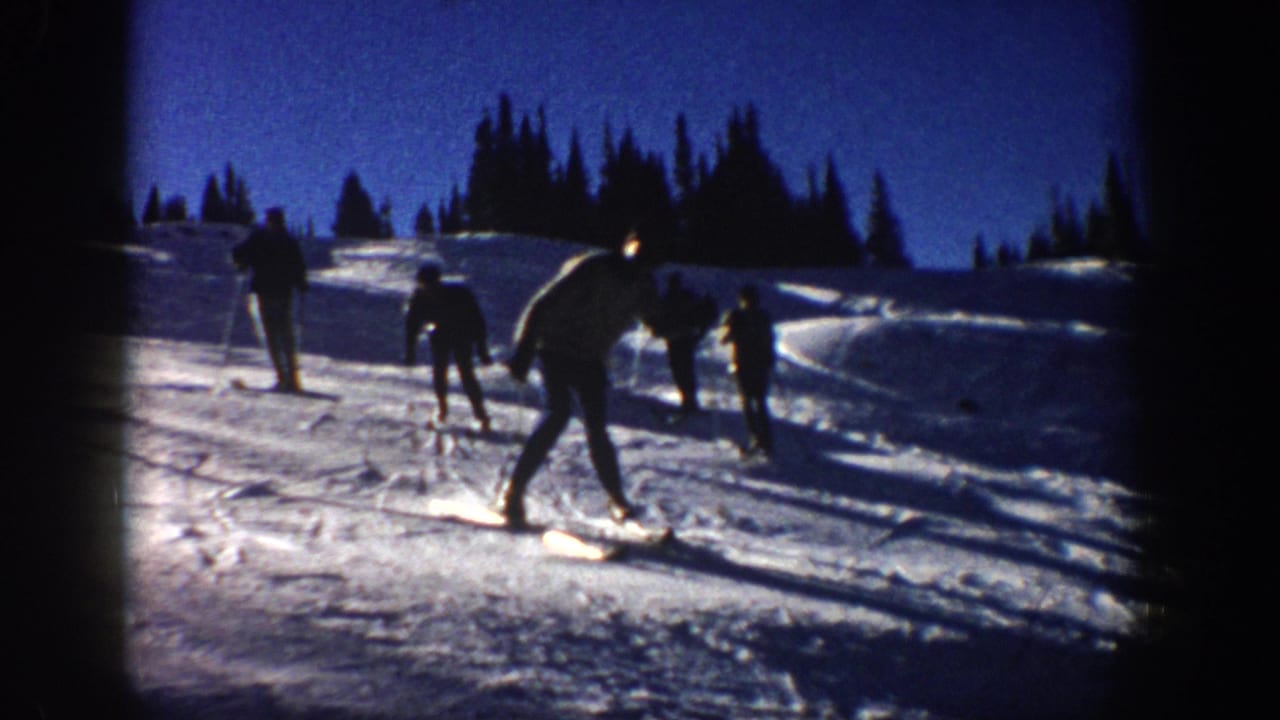 1961 Aspen home-movie frame with a foreground skier leaning into motion and other skiers spread across the slope.