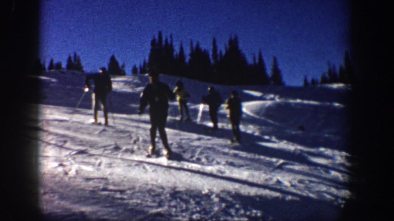 1961 Aspen frame showing skiers spaced across a bright open slope with evergreen trees behind them.
