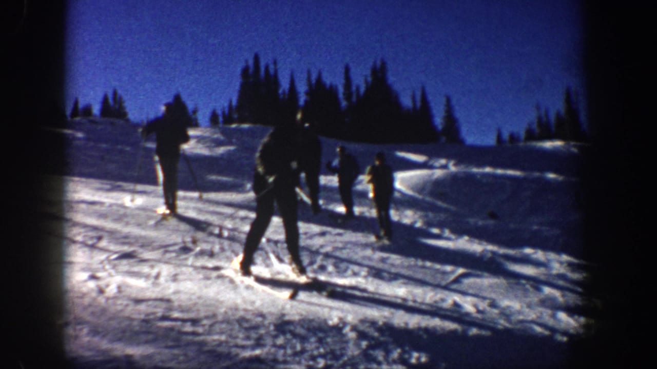 1961 Aspen home-movie frame showing skiers on a snowy mountain slope with evergreen trees and strong 8mm vignetting.