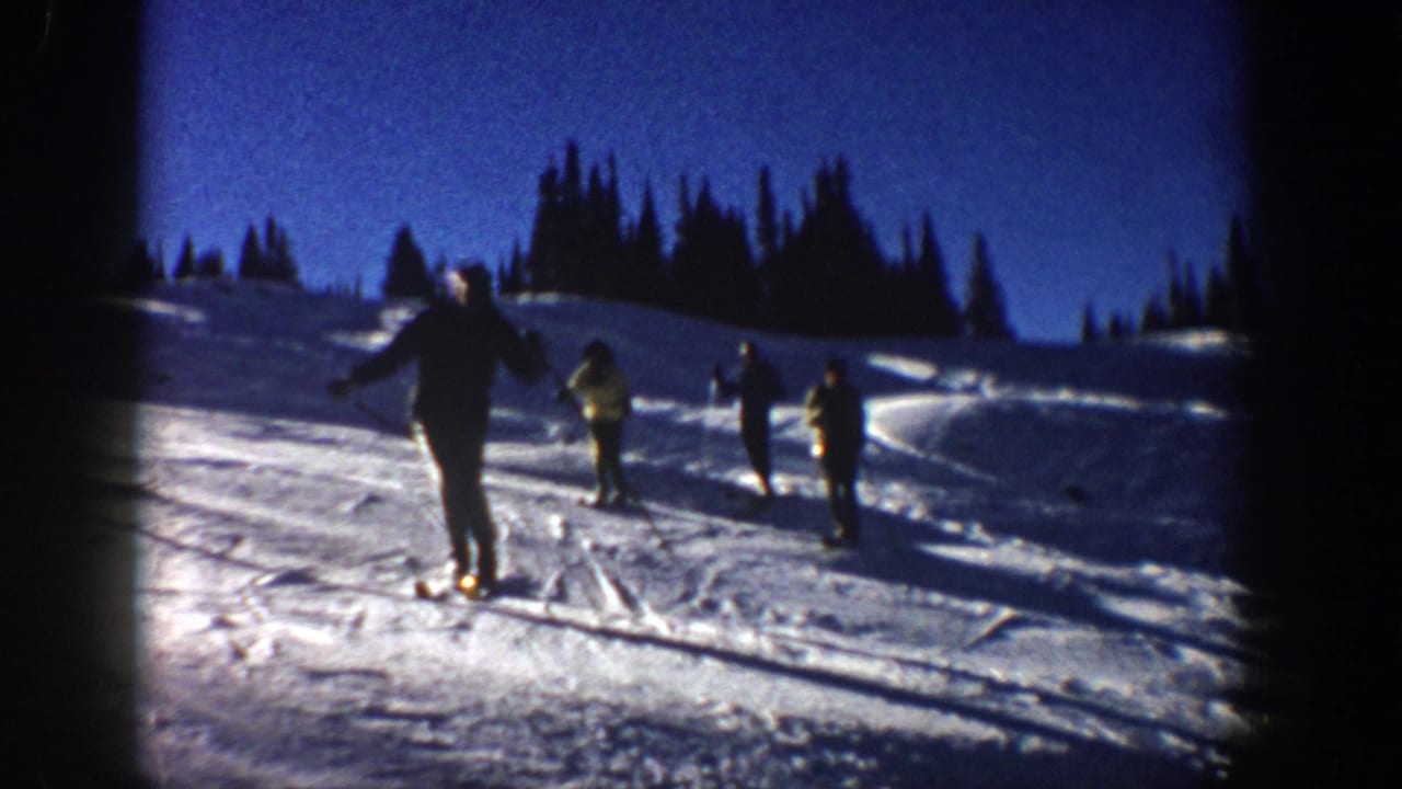 A skier faces downhill while other skiers stand farther across the slope.