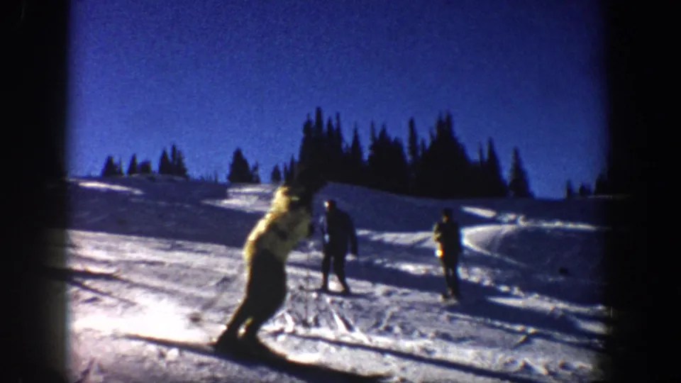 1961 Aspen skiing frame with a skier turning in the foreground, distant figures, tree line, and saturated 8mm color.