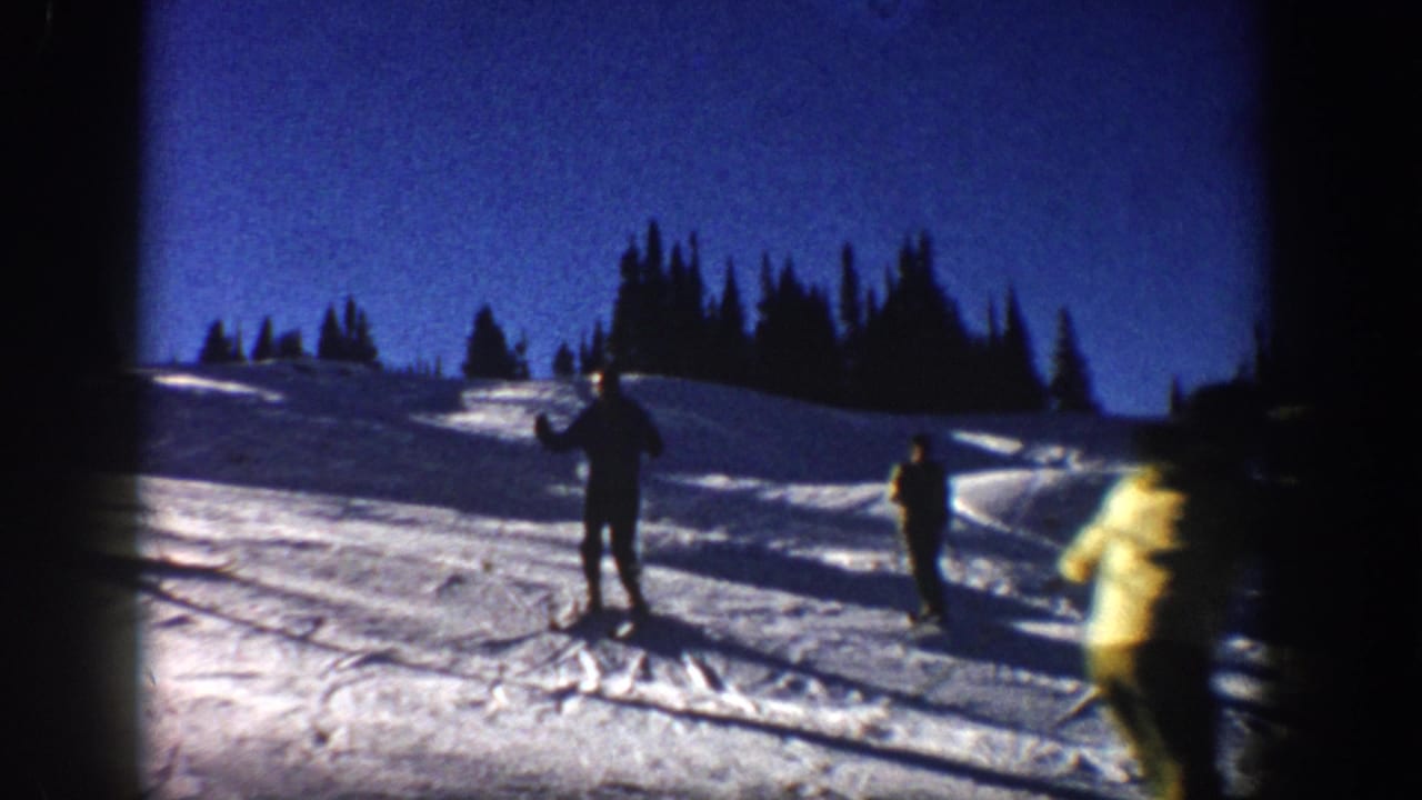 1961 Aspen home-movie frame showing several skiers on a snowy slope with dark evergreen trees and strong winter light.