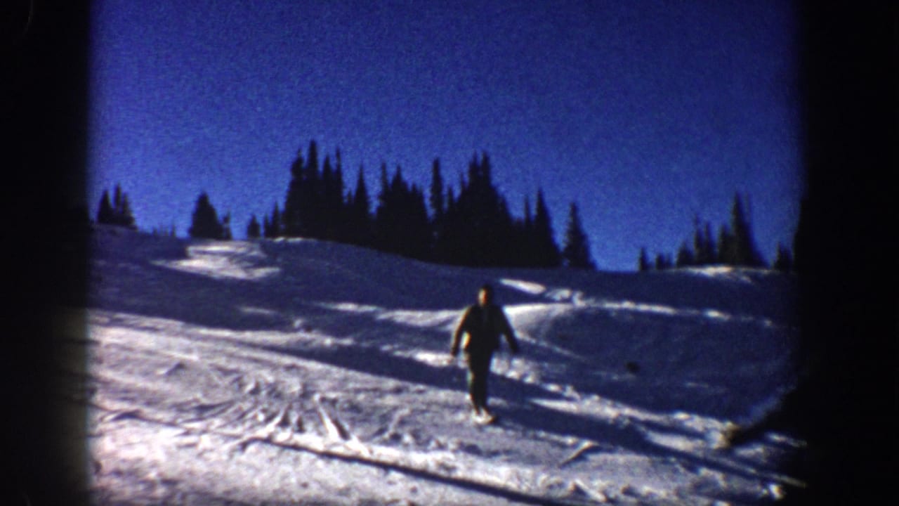 Aspen 1961 home-movie frame showing a skier coming downhill over tracked snow with evergreen trees in the background.