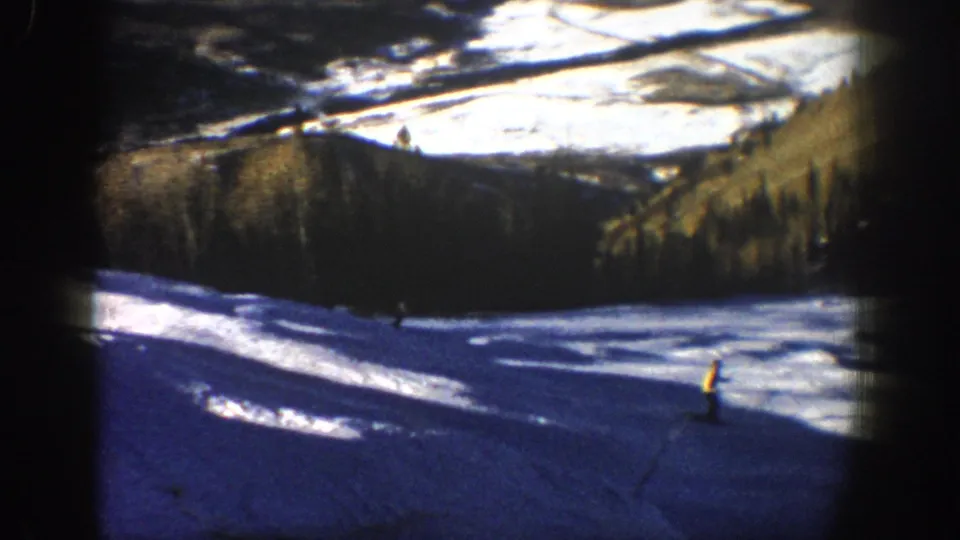 Distant skiers on an Aspen ski slope in 1961, with high-contrast snow, pine trees, and a dark 8mm frame edge.
