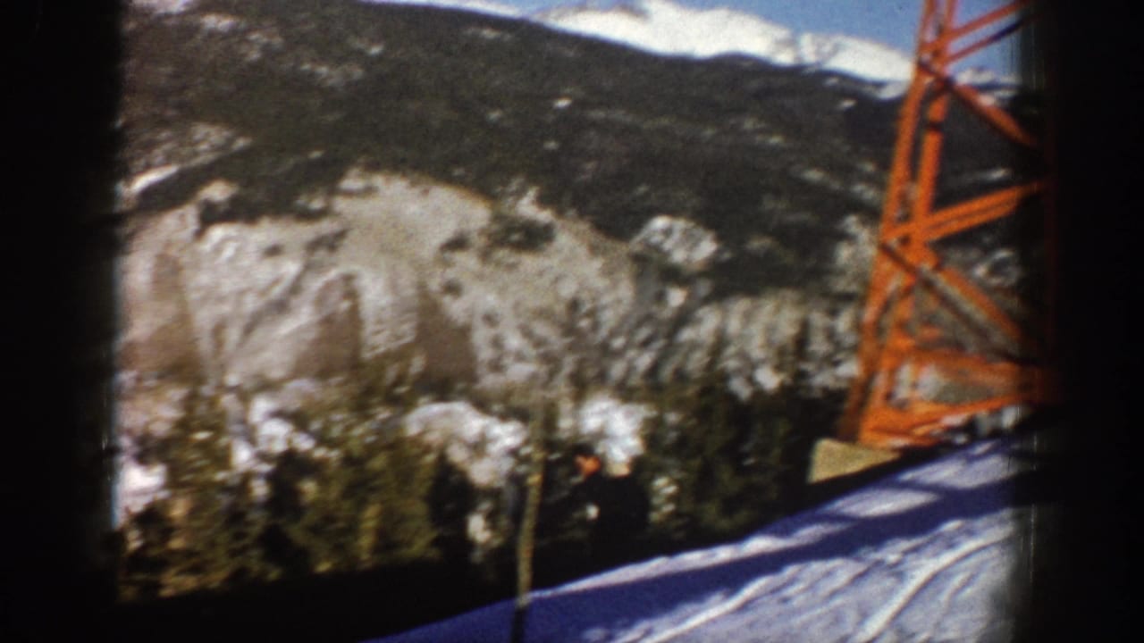 1961 Aspen home-movie frame showing snow, wooded mountainside, and an orange lift tower beside a ski slope.