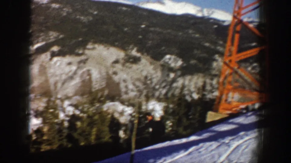 1961 Aspen home-movie frame showing snow, wooded mountainside, and an orange lift tower beside a ski slope.