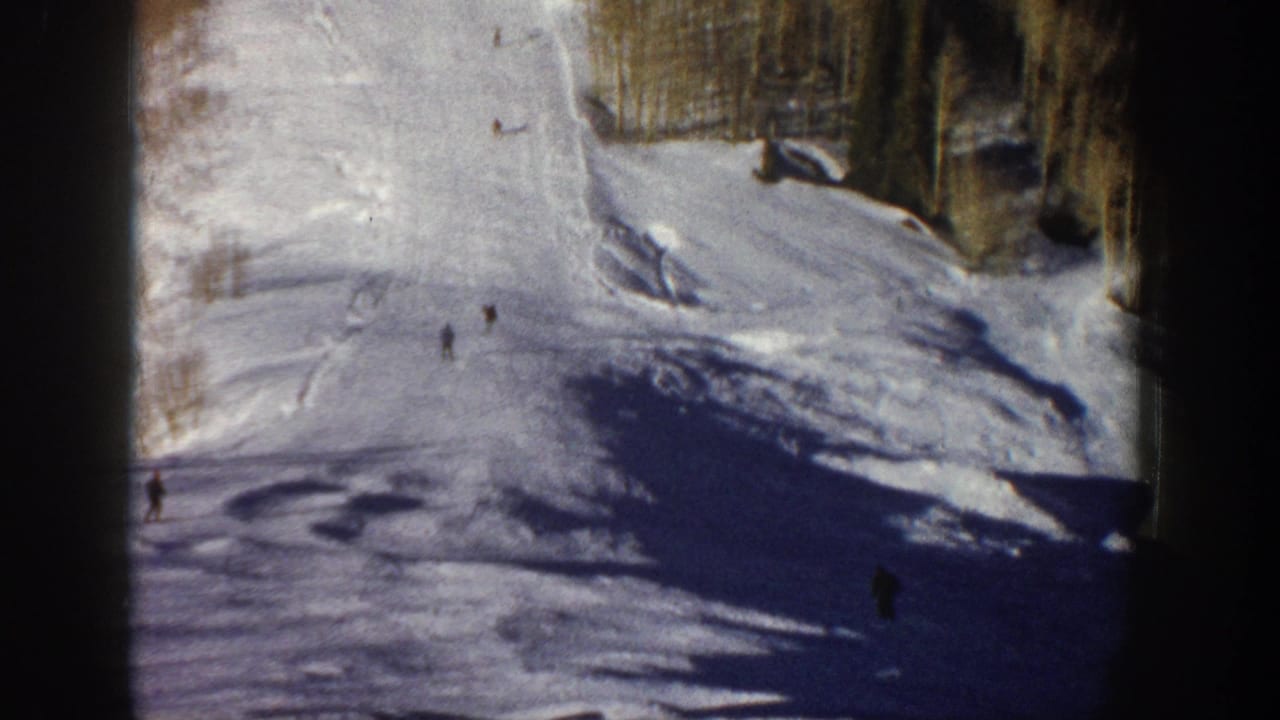 Wide snowy ski run with several small skiers and trees at the top of the slope.