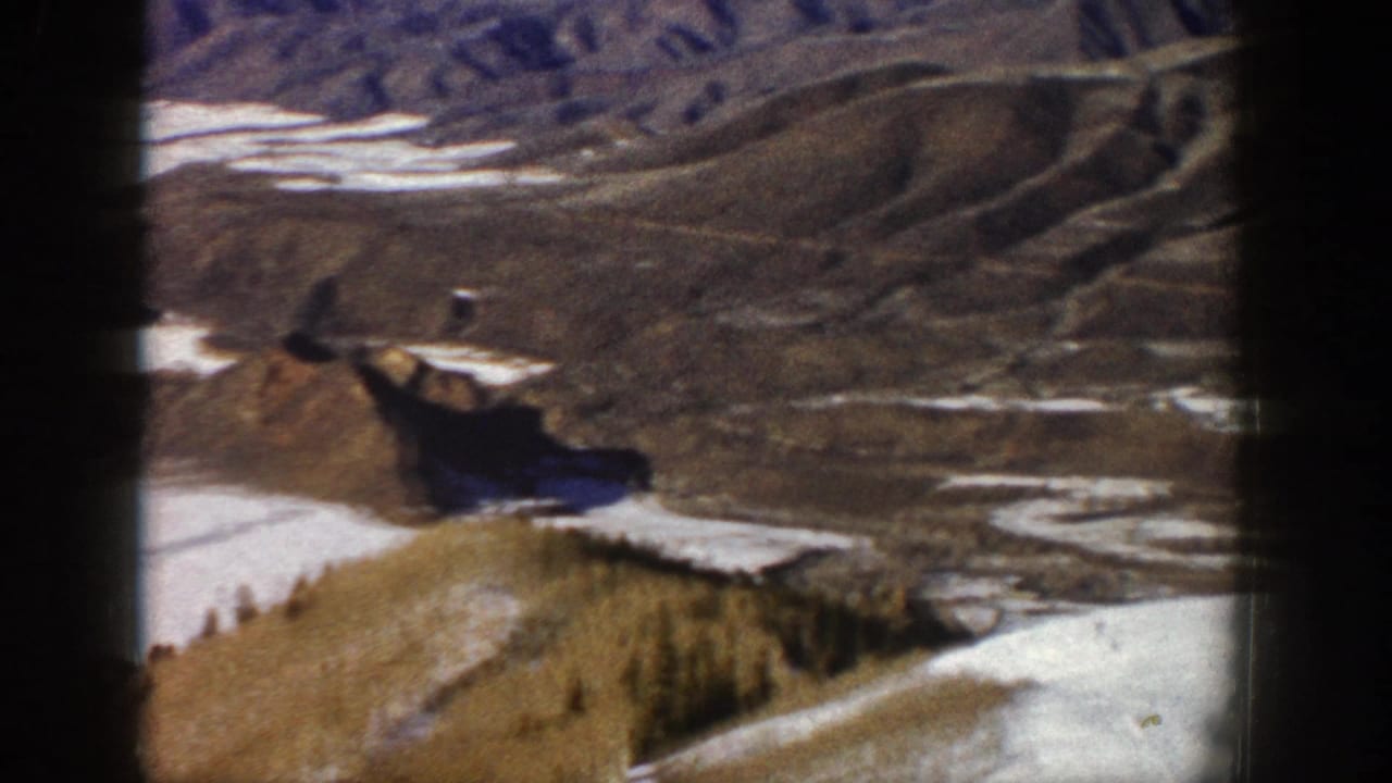 1961 Aspen-area 8mm frame showing a snow-patched valley, brown ridges, and distant mountain terrain.