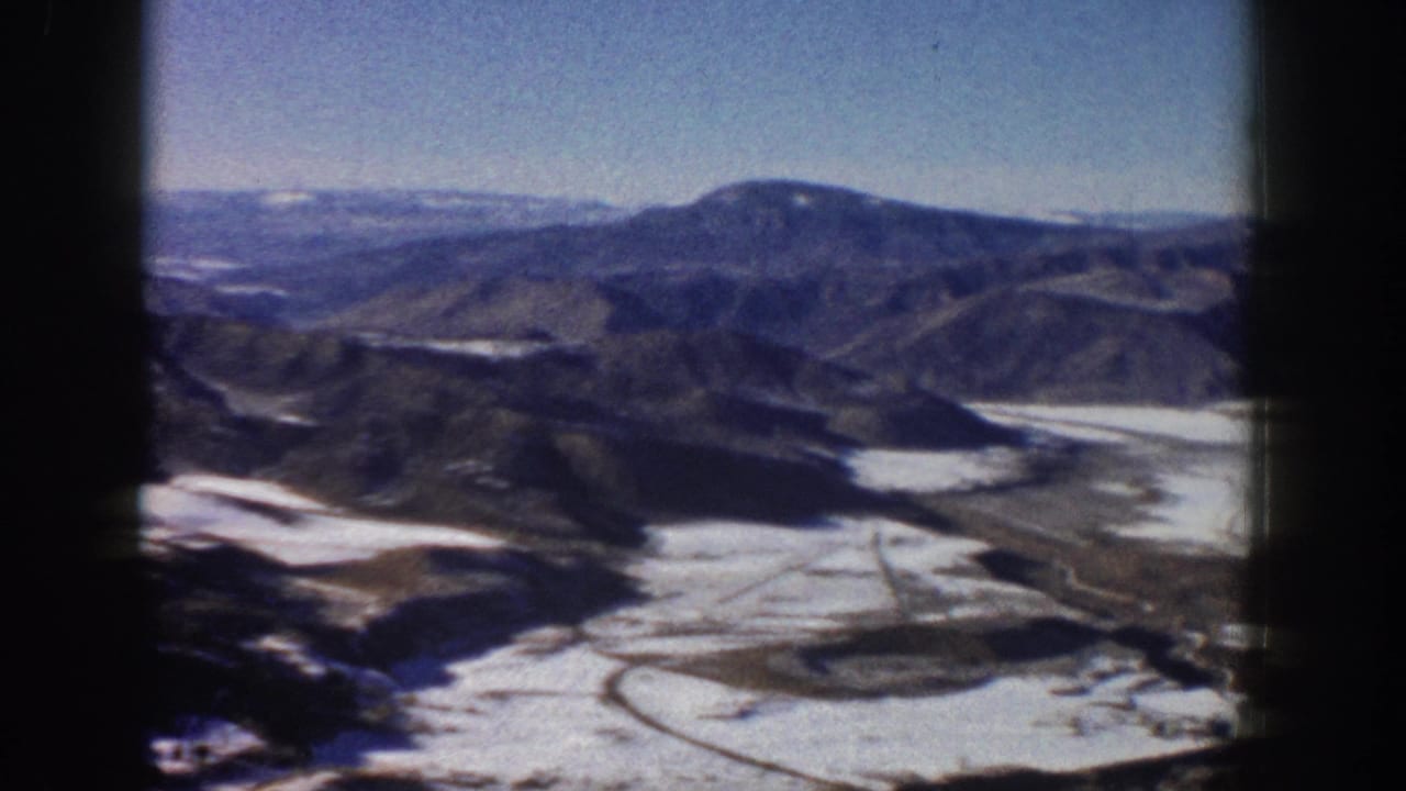 Elevated 1961 Aspen-area view with blue sky, distant mountains, snow patches, and soft 8mm color grain.