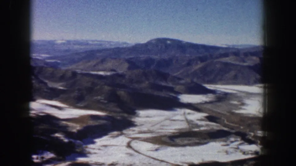 Elevated 1961 Aspen-area view with blue sky, distant mountains, snow patches, and soft 8mm color grain.