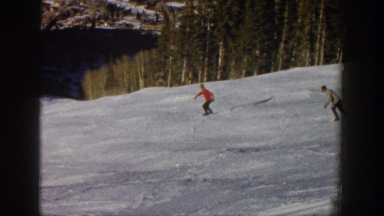 1961 Aspen ski-trip frame showing two distant skiers, including one in red, descending a snowy slope near trees.