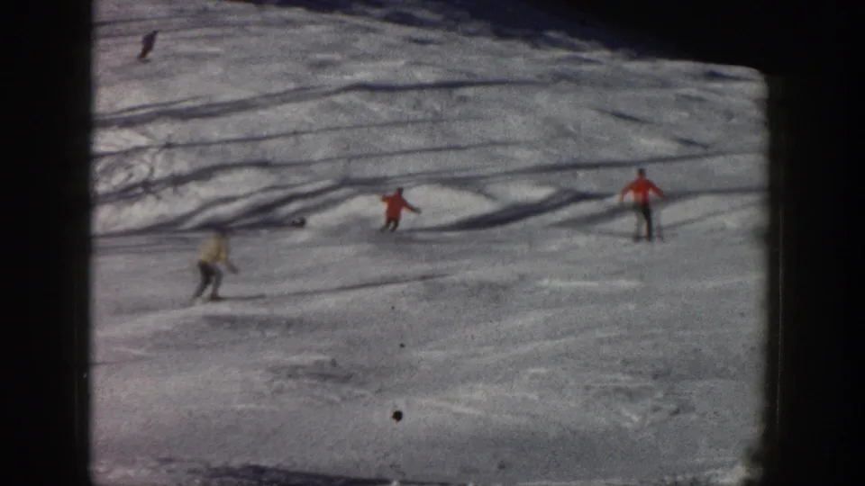 1961 Aspen, Colorado home-movie frame showing distant skiers in colored coats moving down a bright snowy slope.