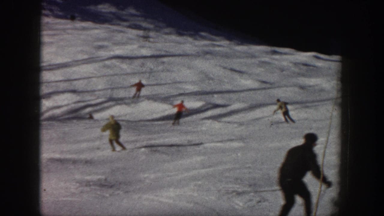 Vintage 8mm frame of recreational skiers descending an Aspen slope, with a dark foreground figure entering at right.