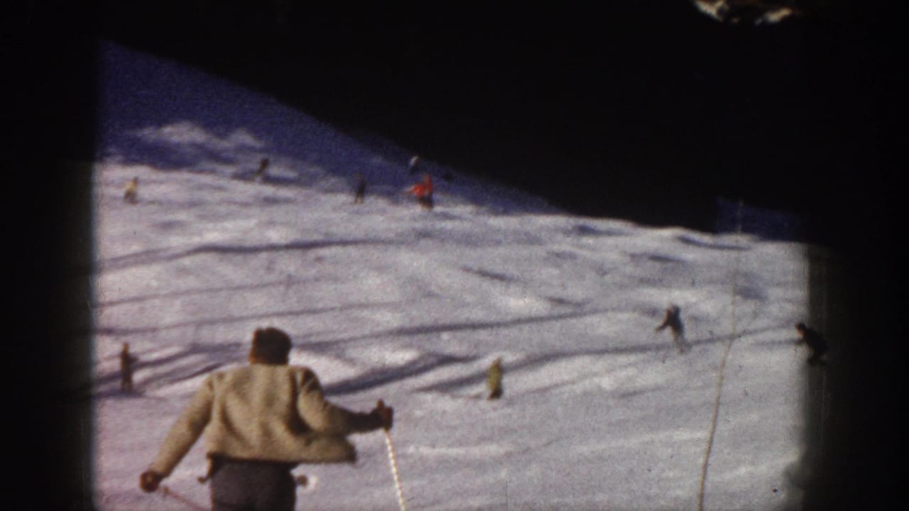 A skier in a light jacket descends behind other skiers on a snowy slope.