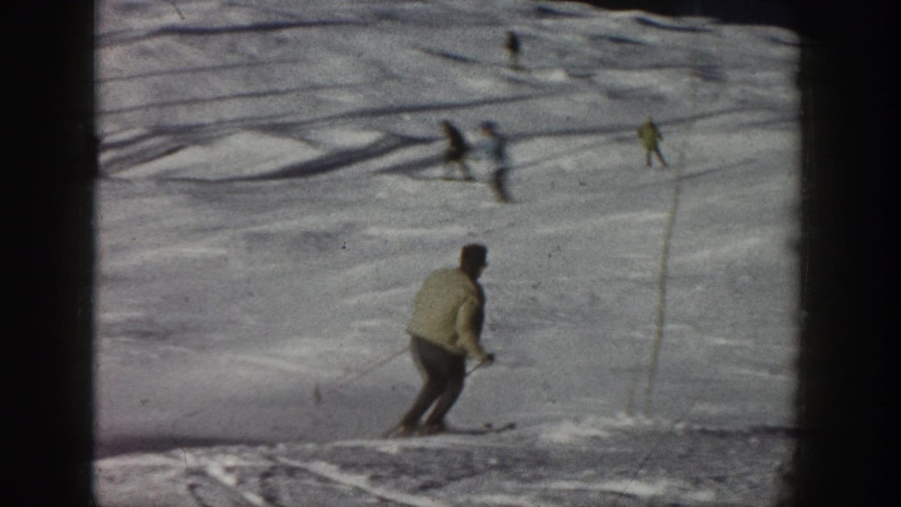1961 Aspen home-movie view of a skier near the lower edge of the frame, with poles or markers and distant skiers on the snow.
