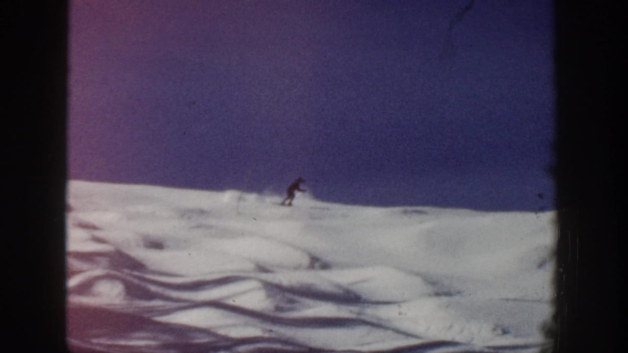 A distant skier traverses open snow in Aspen, Colorado 1961 footage, with purple-blue shadowing and visible 8mm frame borders.