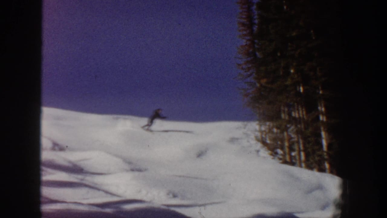 1961 Aspen 8mm frame showing a distant skier zigzagging across snow with evergreens to the right.