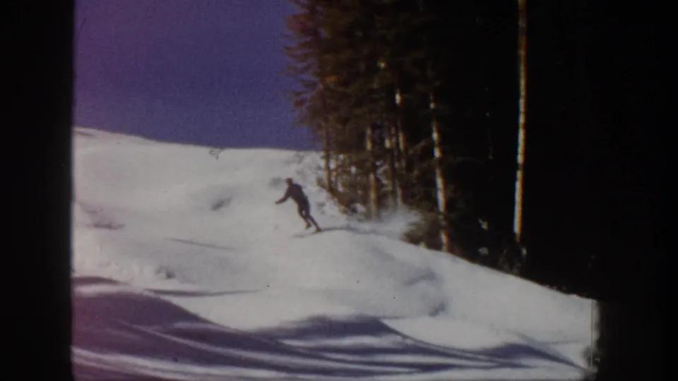 1961 Aspen 8mm frame showing a lone skier on a snow-covered slope near dark evergreen trees.