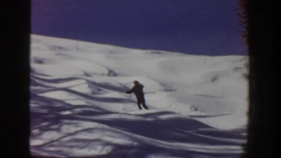 1961 Aspen footage shows the skier farther down the snowy slope, framed by shadow patterns and visible film borders.