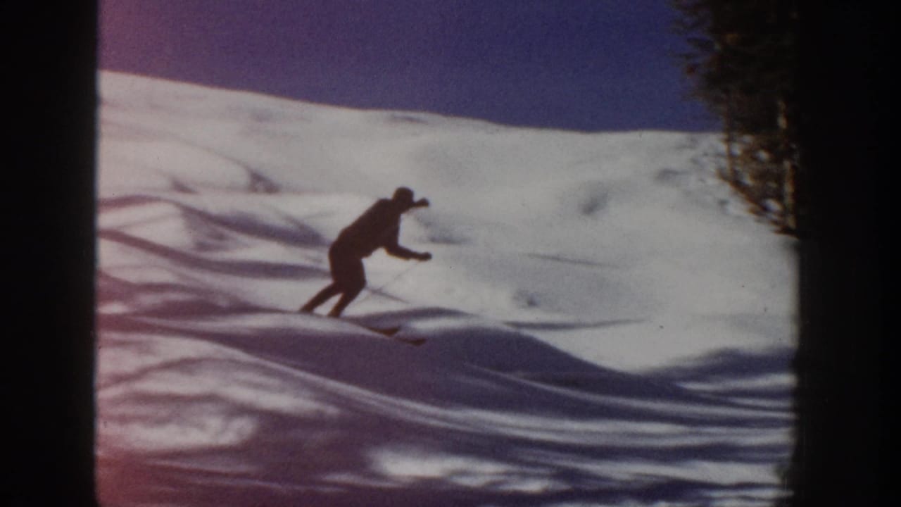 The lone skier leans into the descent on an Aspen snow slope, with evergreen trees and dark film edges visible.