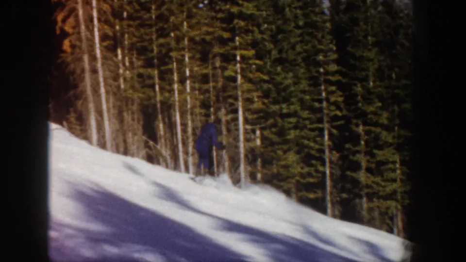 A distant skier in dark clothing moves across an Aspen, Colorado snow slope in 1961 home-movie footage.