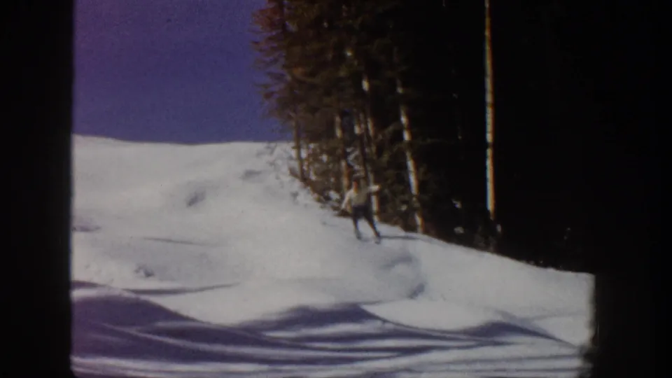 The skier reaches the lower right of the snowy slope near the forest in 1961 Aspen home-movie footage.