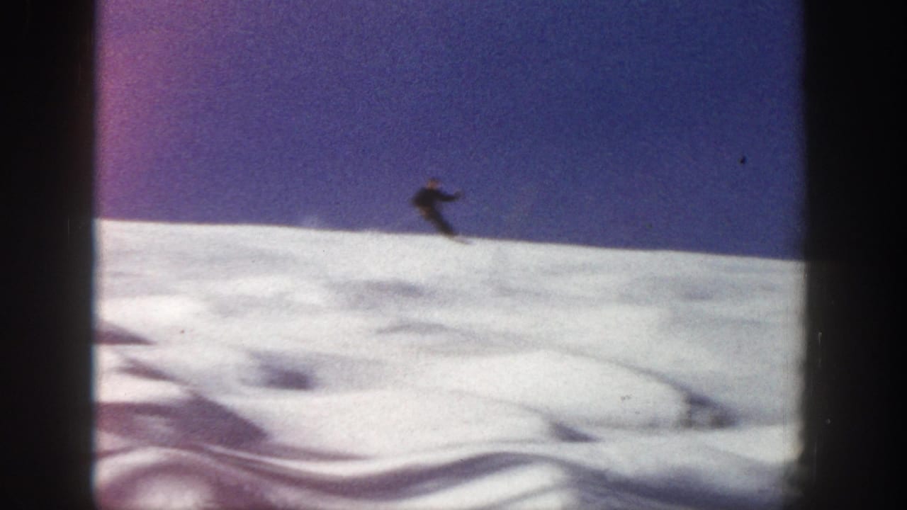 Distant skier on an Aspen, Colorado snow slope in 1961 8mm home-movie footage, seen beneath a deep blue sky.