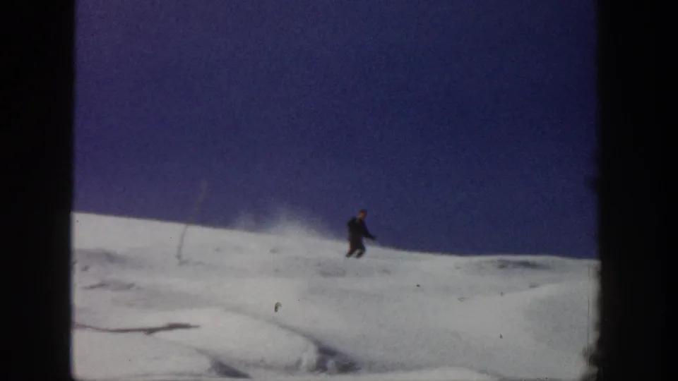 A distant skier moves along open snowy terrain in the Aspen 1961 home-movie clip, framed by dark 8mm borders.