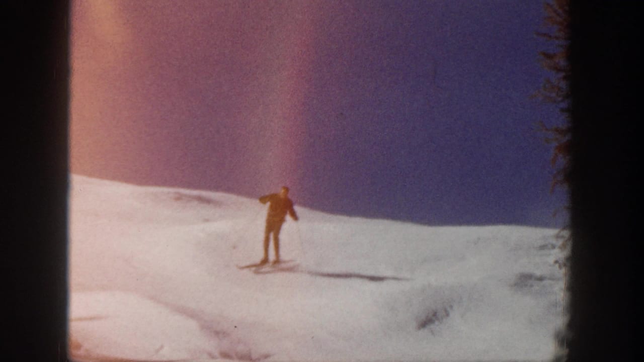 A lone skier in Aspen, Colorado, 1961, moves across an open snow slope under a purple-blue sky in soft 8mm color.