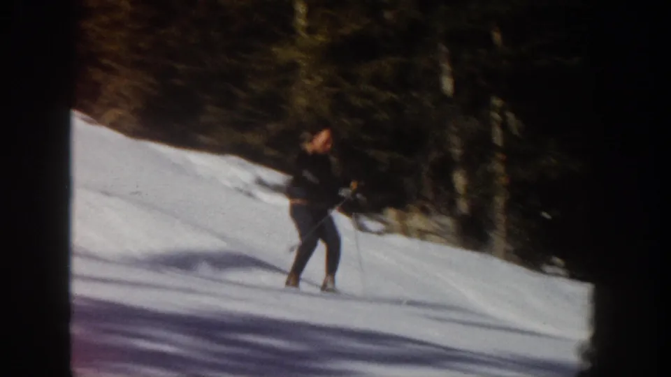 The skier slows beside the wooded edge of the Aspen slope, with long shadows across the snow and visible 8mm frame softness.