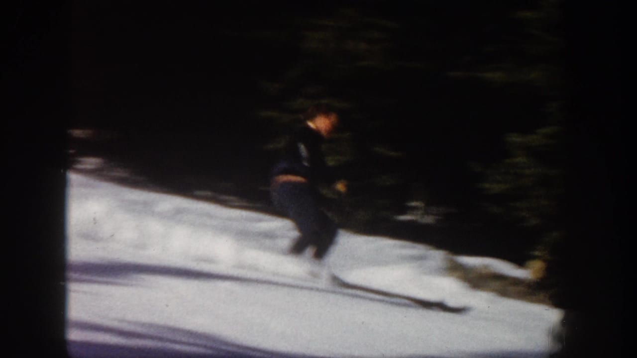 1961 Aspen home-movie frame showing a skier descending a snow-covered slope near dark evergreen trees.