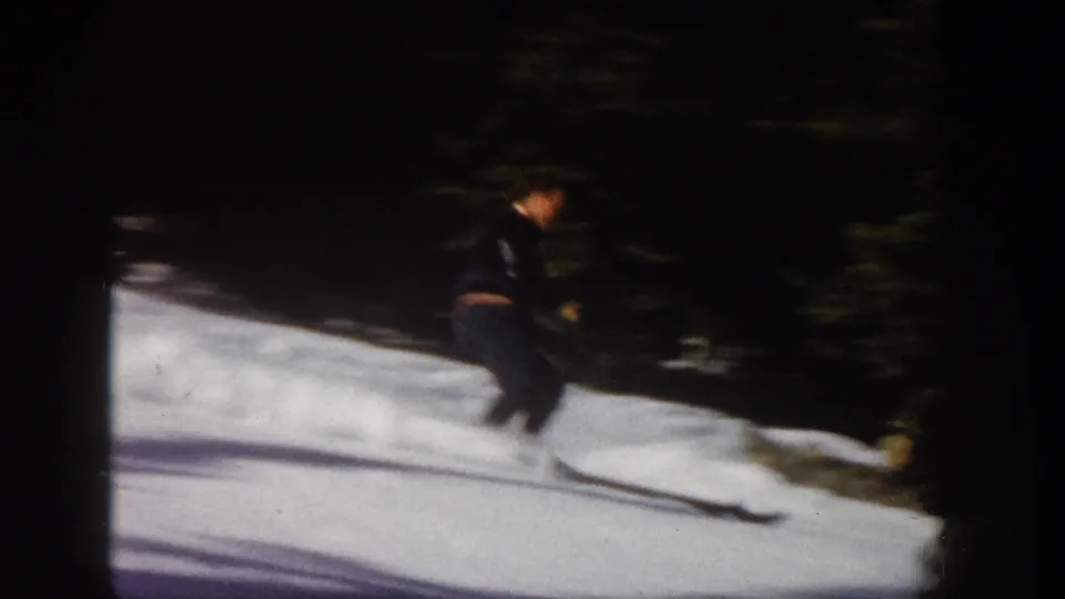 1961 Aspen home-movie frame showing a skier descending a snow-covered slope near dark evergreen trees.