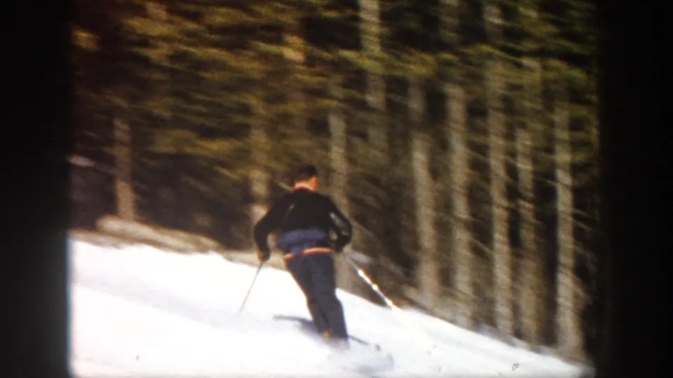 Skier in dark clothing moves downhill through an Aspen, Colorado forested ski slope in 1961 footage.