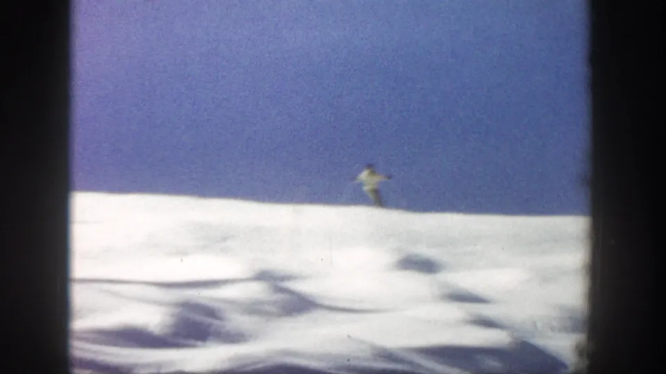 Wide 1961 Aspen skiing view with a small distant skier on a sunlit snow ridge below blue sky.