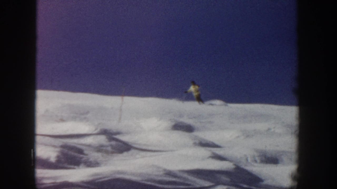 Distant skier crosses a snow-covered Aspen slope in supported 1961 home-movie footage, framed by dark 8mm borders.