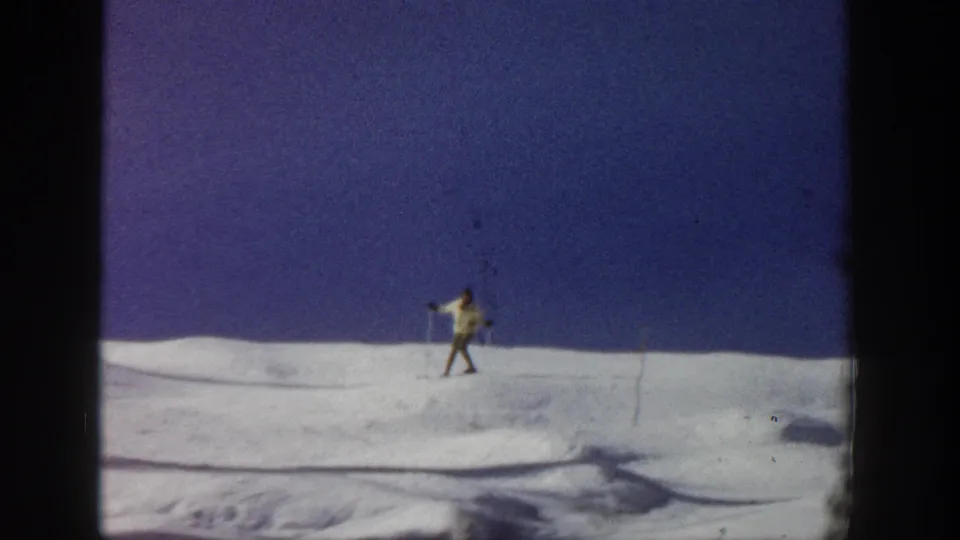 The skier appears lower in the frame on the Aspen snowfield, holding poles against a wide blue-sky background.