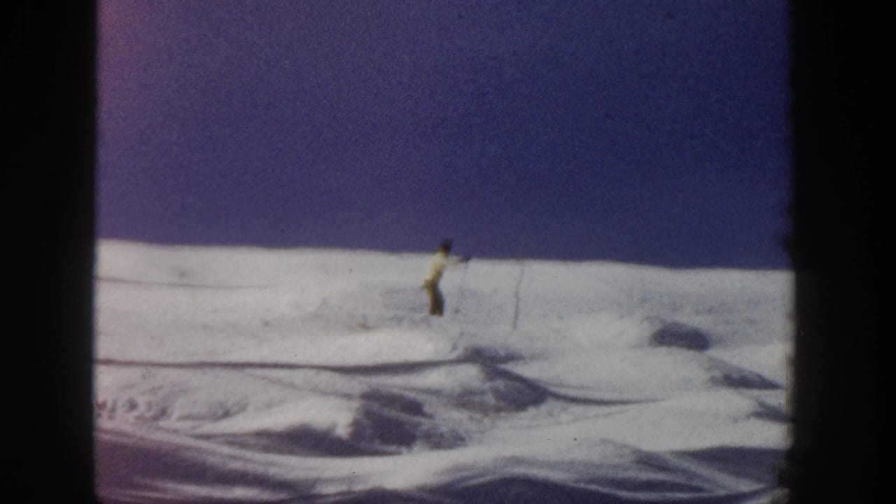 Lone skier on a snowy slope beneath a dark purple sky.