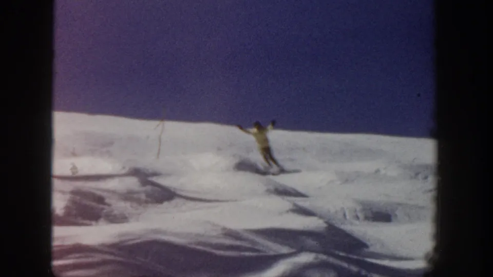 A skier in a light jacket uses poles while moving across a snowy Aspen slope in 1961 home-movie footage.