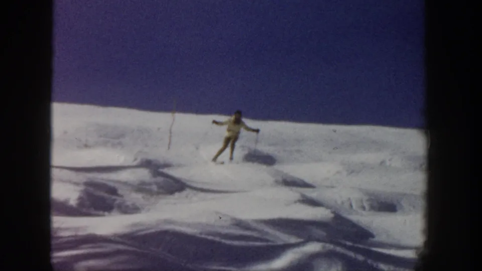 A lone skier appears mid-descent on a bright snow-covered Aspen hillside, filmed on 8mm in 1961.