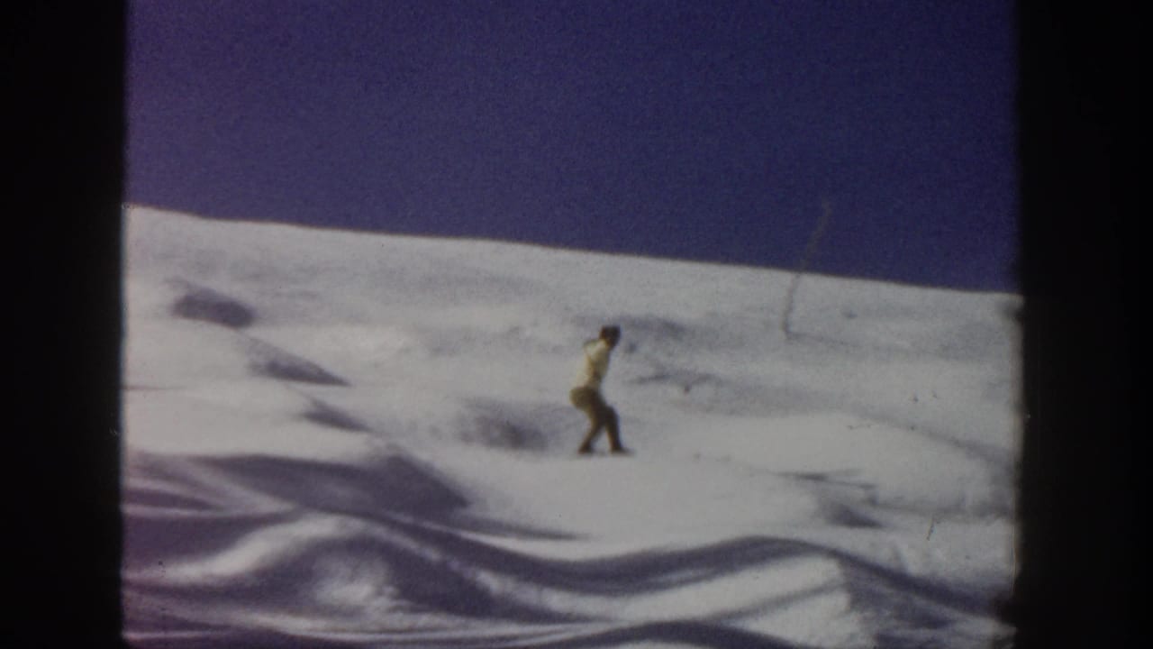 A distant skier moves across an Aspen snow slope in 1961 8mm home-movie footage, framed by dark film borders.