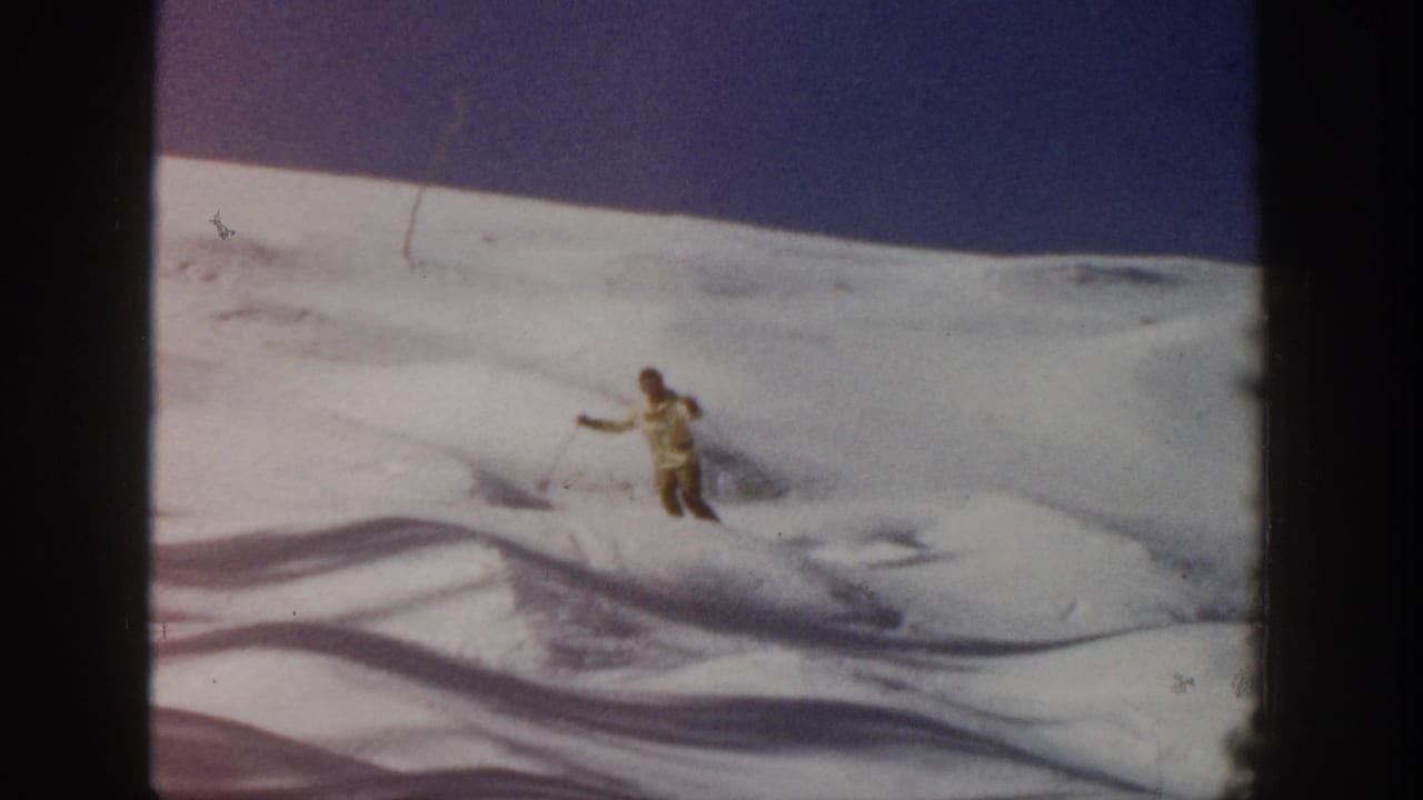 Skier descending across uneven snow with poles visible.