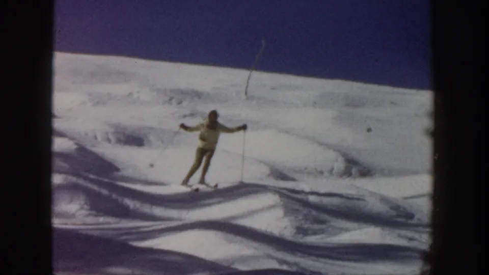 A lone skier faces toward the camera on an open Aspen slope, arms out with ski poles in a home-movie frame.