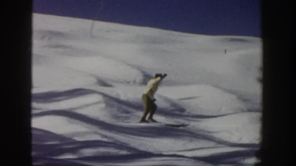 The skier leans into motion across the snow in a 1961 Aspen home-movie shot with soft focus and visible film wear.