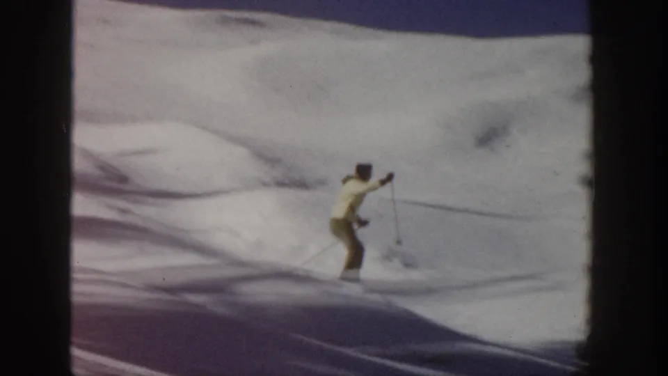 In supported 1961 Aspen footage, a skier in yellow outerwear glides across open snow with long shadows and soft 8mm blur.