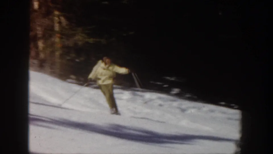 A distant skier in yellow and olive clothing leans into the descent on a sunlit Colorado ski slope, captured with soft motion blur.